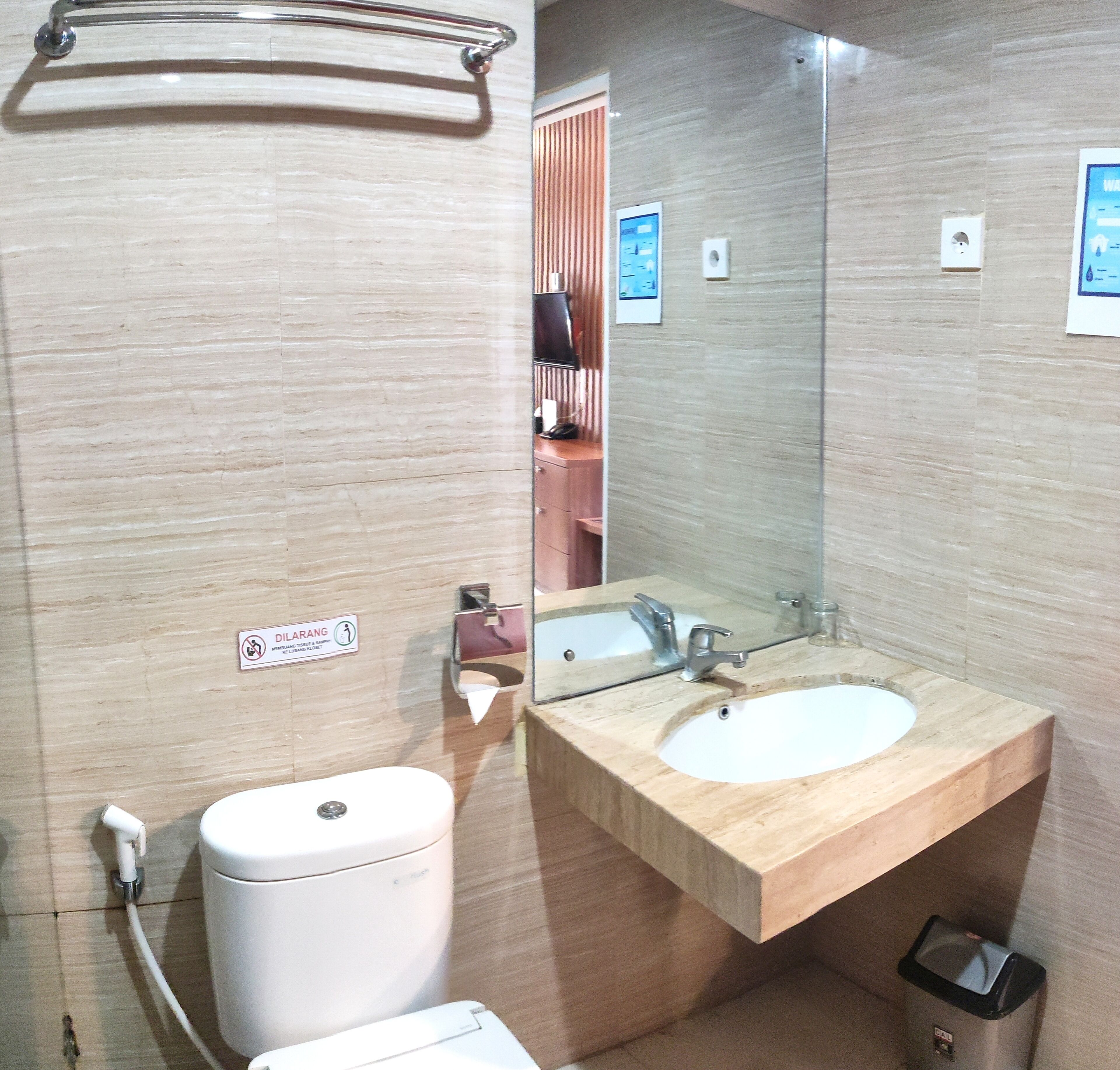 Baño con inodoro, lavabo y espejo. Hay un cartel en la pared y un perchero sobre el lavabo.