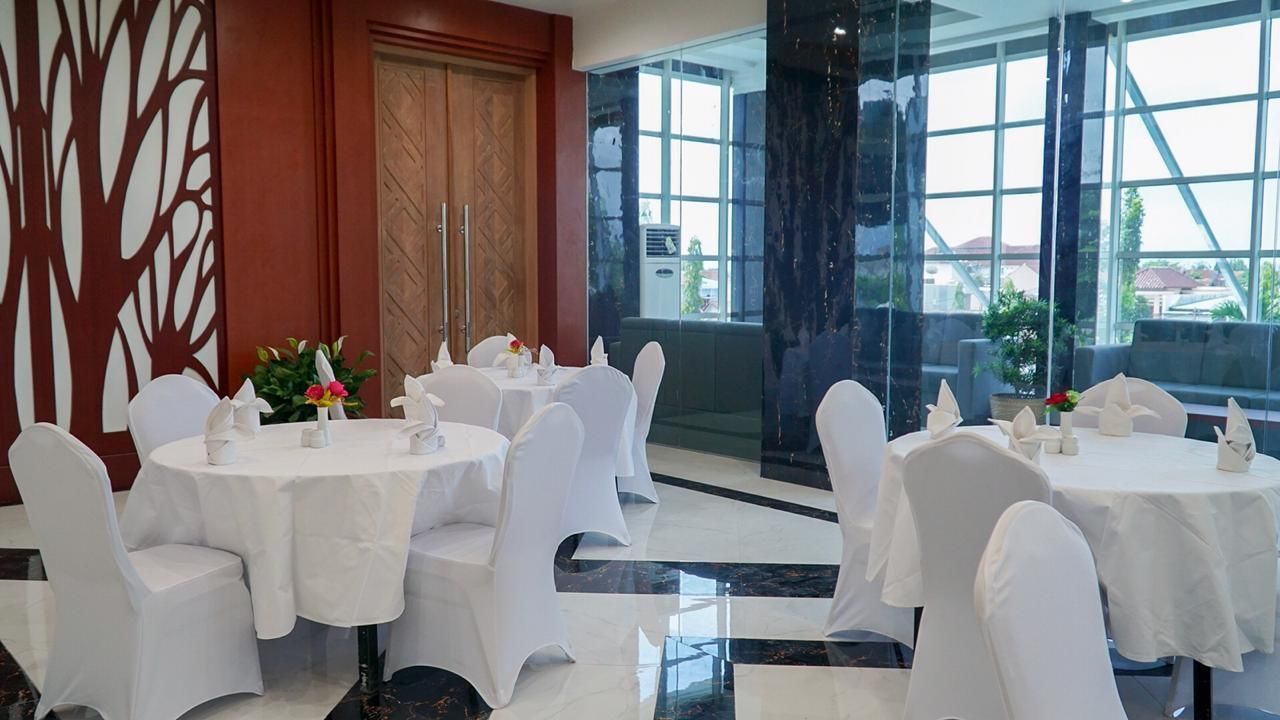 A dining area with round tables and white chairs, large windows, and a decorative wall.