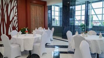 A dining area with round tables and white chairs, large windows, and a decorative wall.