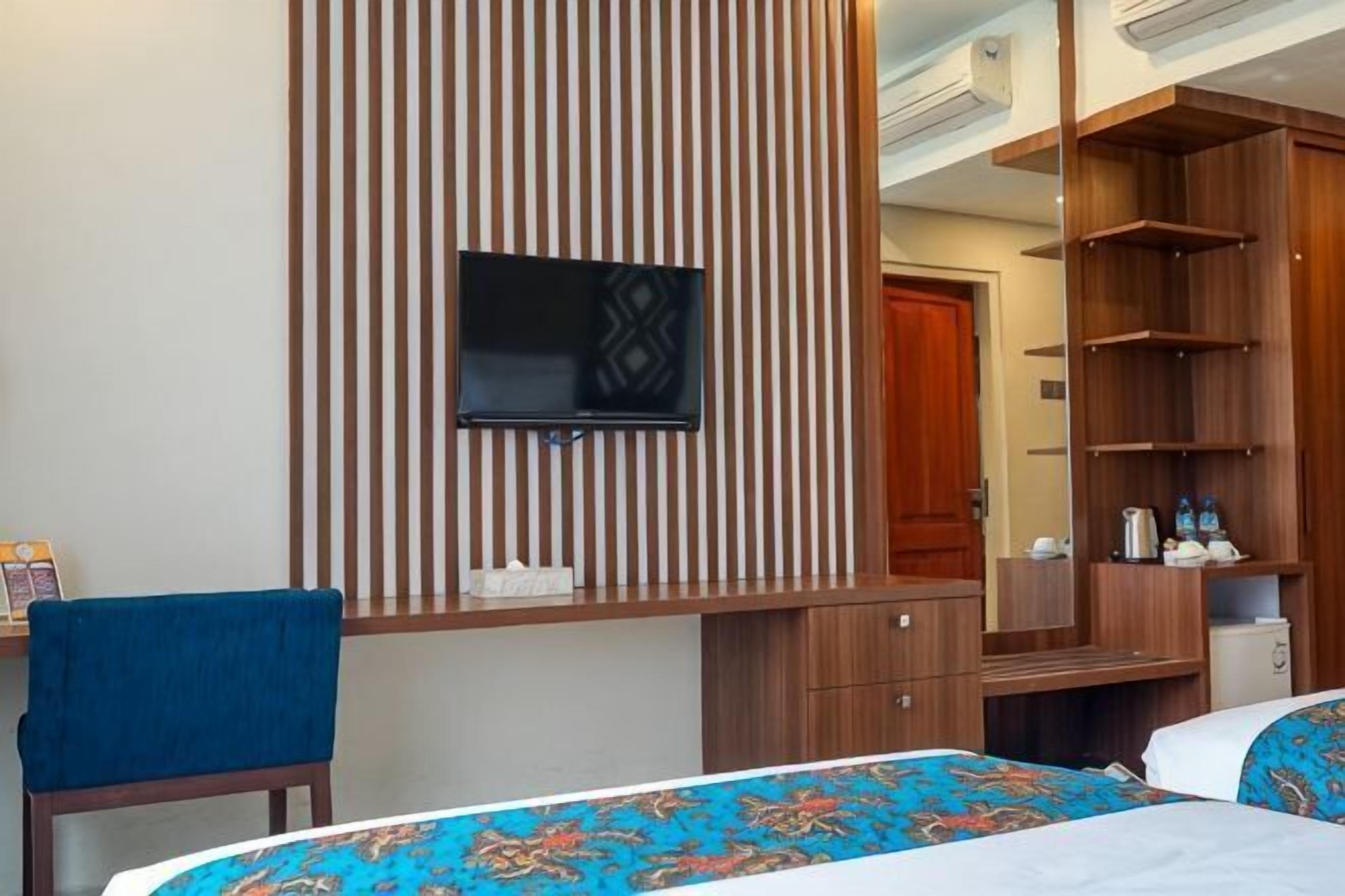 Een hotelkamer met een bed, een bureau met stoel, een aan de muur bevestigde televisie en een kledingkast.