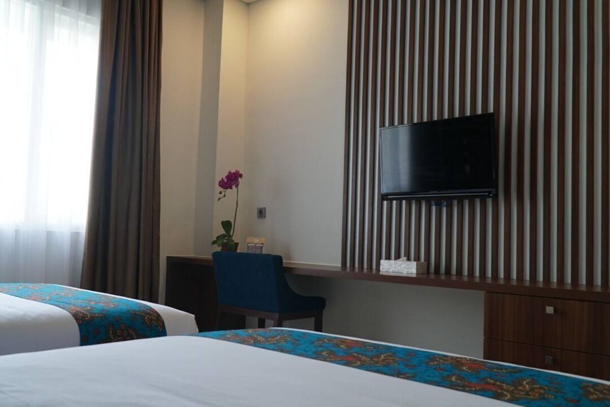 Habitación de hotel con dos camas, un escritorio, una silla, un televisor montado en la pared y una ventana con cortinas.