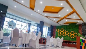Um hall de hotel moderno com mesas redondas, cadeiras brancas e uma parede verde com padrões hexagonais.