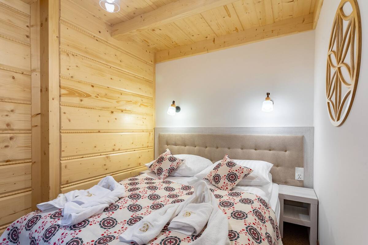 A wooden-paneled room with a bed, two wall-mounted lights, and a decorative wall piece.