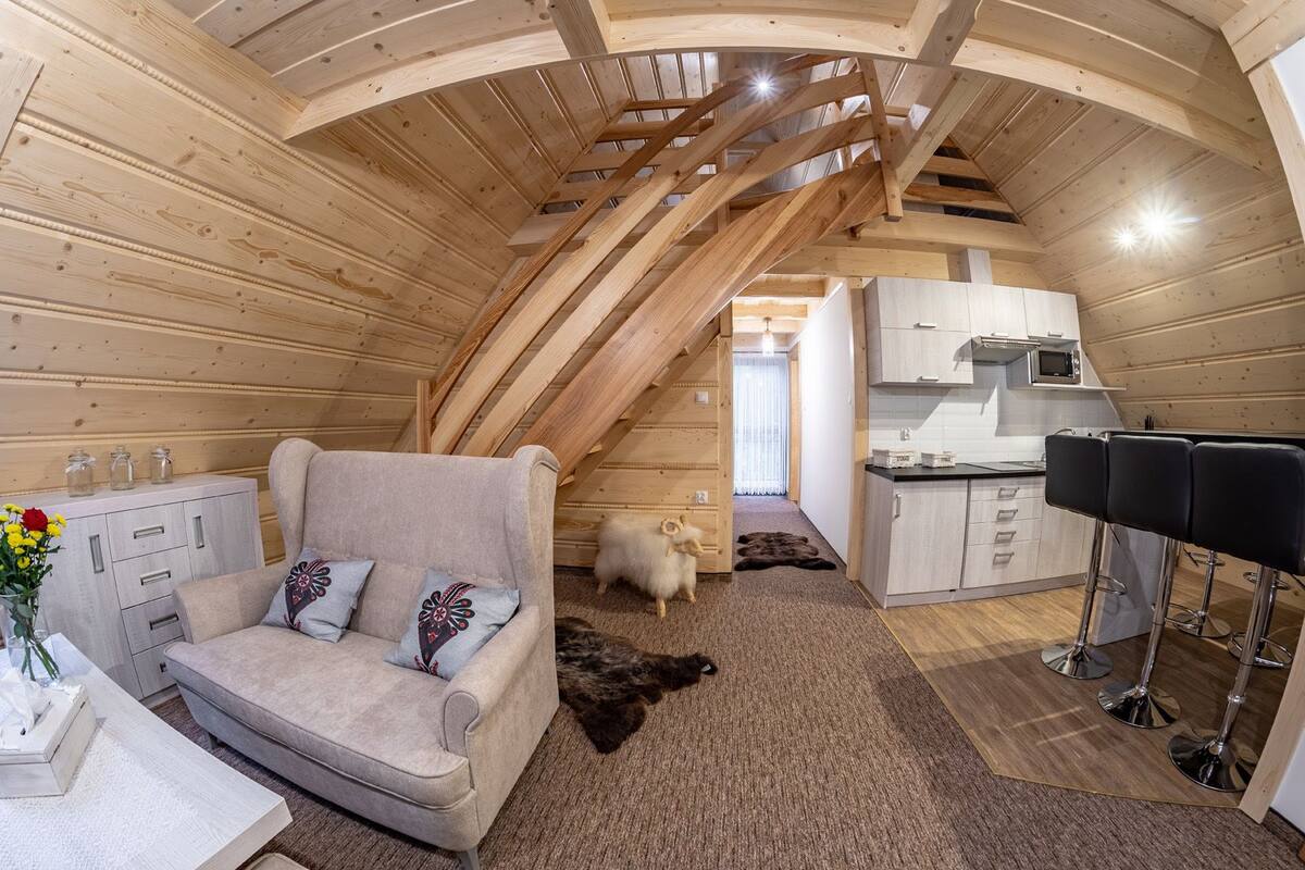 A cozy attic room with a sofa, a small kitchen, and a dog.