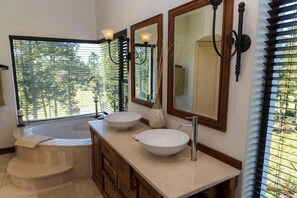 A bathroom with two large sinks, a bathtub, and a window with blinds.
