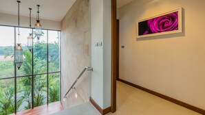 Una escalera moderna con barandas de vidrio, vistas al verdor exterior y una obra enmarcada en la pared.