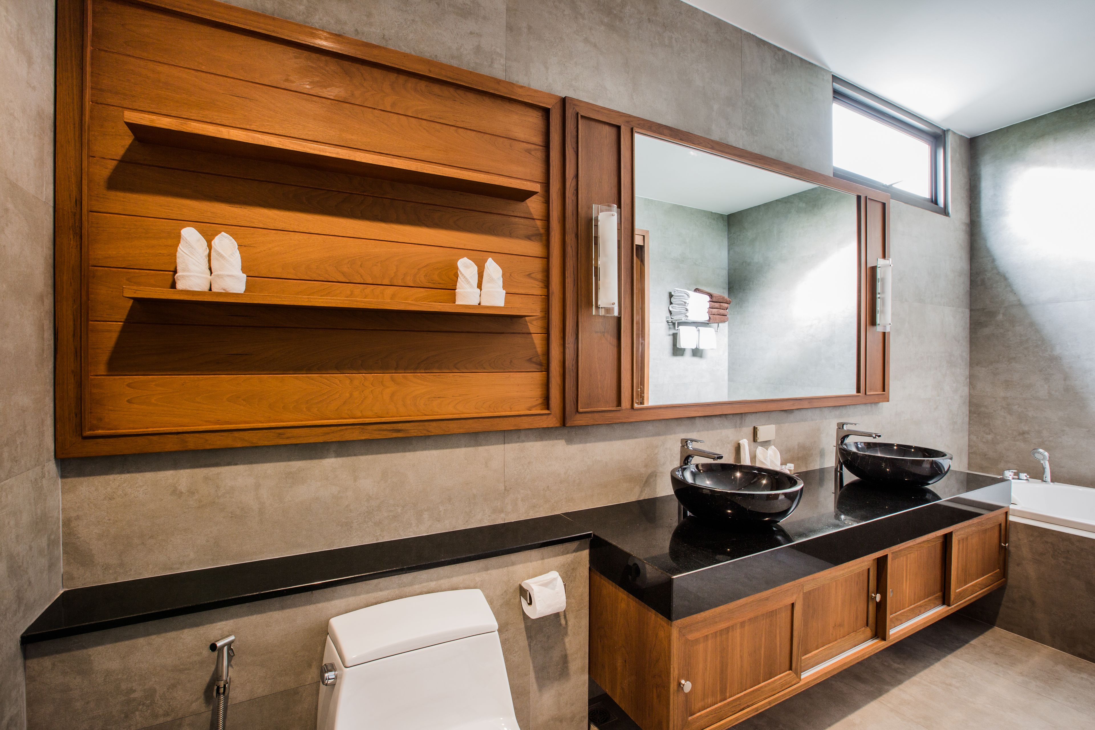 A modern bathroom with wooden cabinets, a black countertop, a large mirror, and a black vessel sink.