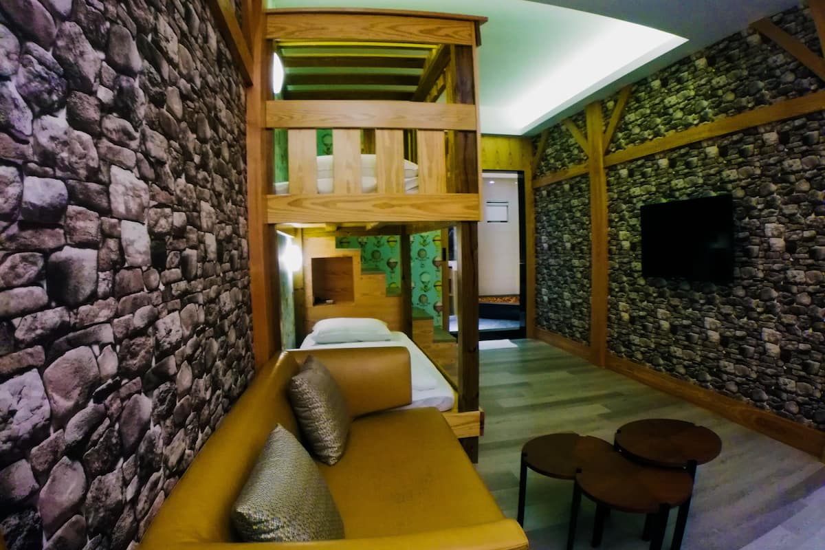 A room with a stone wall, a wooden bunk bed, a yellow sofa, and a flat-screen TV mounted on the stone wall.