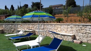 Un área junto a la piscina con sillas de descanso y sombrillas a rayas.
