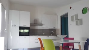 Una cocina moderna con armarios blancos, horno empotrado y comedor con sillas de colores.