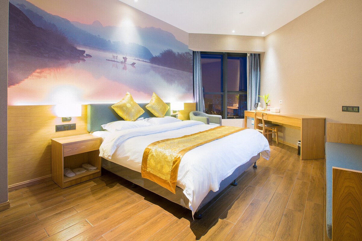 Ein modernes Hotelzimmer mit einem großen Bett, einem Schreibtisch, einem Sessel und Blick auf eine gebirgige Landschaft.