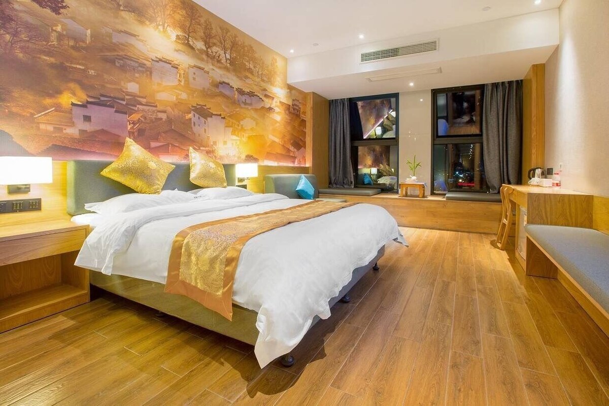 Ein geräumiges Hotelzimmer mit einem großen Bett, Holzböden, Blick auf die Stadt und moderner Einrichtung.