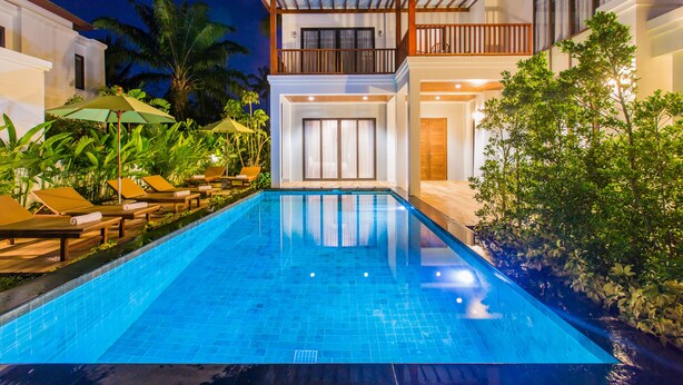 A swimming pool with lounge chairs and umbrellas, surrounded by tropical plants and a two-story building with balconies. - Villa Palavee B3 (Krabi)