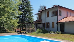 A swimming pool with a pergola, a house with a red-tiled roof, and a garden with trees and shrubs. - Villa Cristina (Vicchio)
