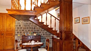 A dining area with a wooden staircase, stone wall, and a table set with chairs. - Villa Cristina (Vicchio)