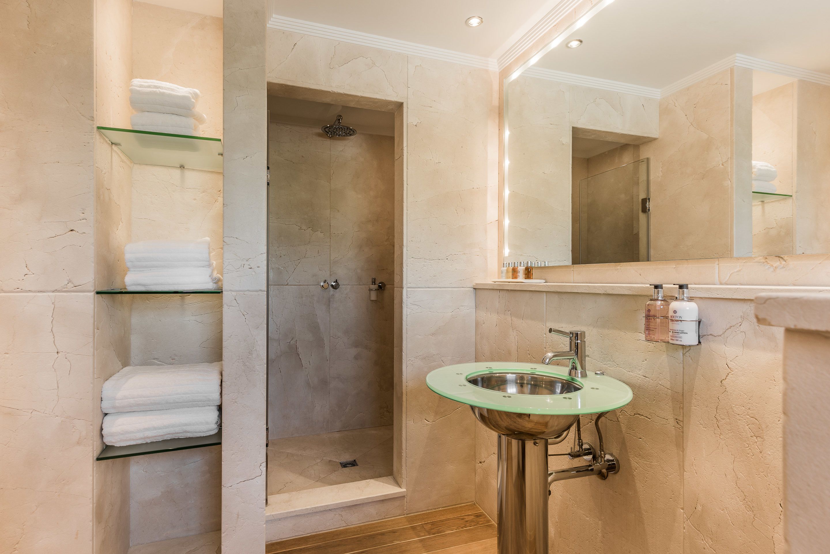 Un baño moderno con cabina de ducha de vidrio, un lavamanos con detalle verde y un pared con azulejos de mármol.
