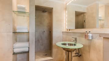 Un baño moderno con cabina de ducha de vidrio, un lavamanos con detalle verde y un pared con azulejos de mármol.