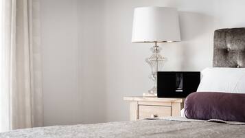 Un lit bien fait, avec un oreiller blanc et un oreiller violet, une table de chevet avec une lampe et un haut-parleur posé sur la table.