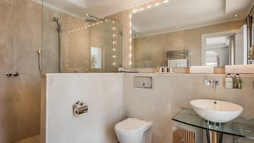 Un baño moderno con ducha envuelta en vidrio, inodoro blanco y lavamanos de vidrio.