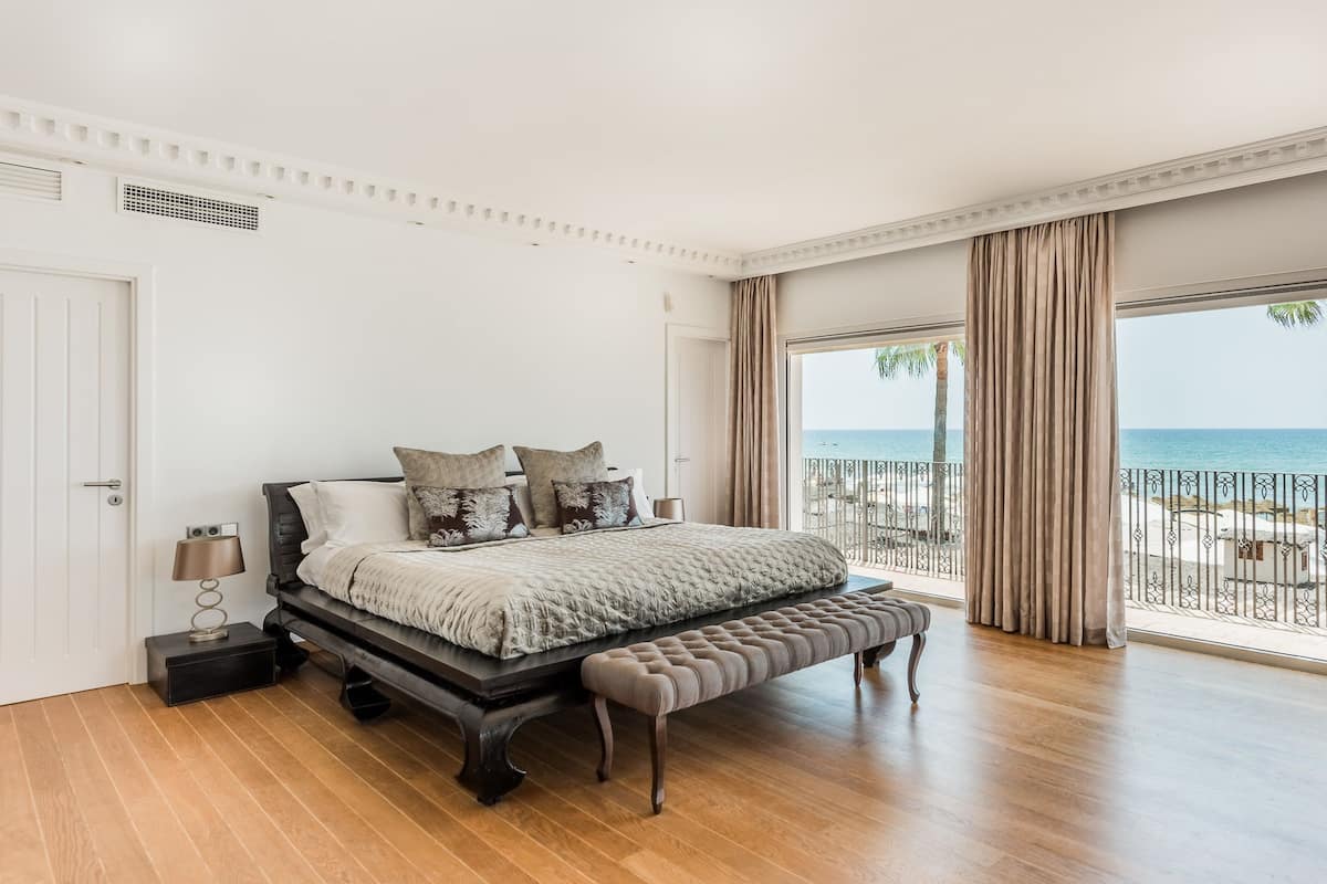 Une chambre avec un grand lit, un banc, une table de chevet et une vue sur la plage.