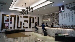 Ein Hotel-Empfangsbereich mit modernem Design, der eine Rezeption, eine Sitzecke und eine Wand mit dekorativen Elementen umfasst.