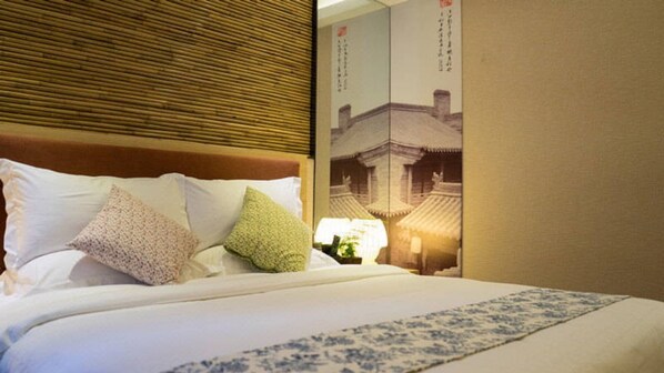 A neatly made bed with white linens and decorative pillows, a wooden headboard, and a wall with a traditional Chinese architectural poster.