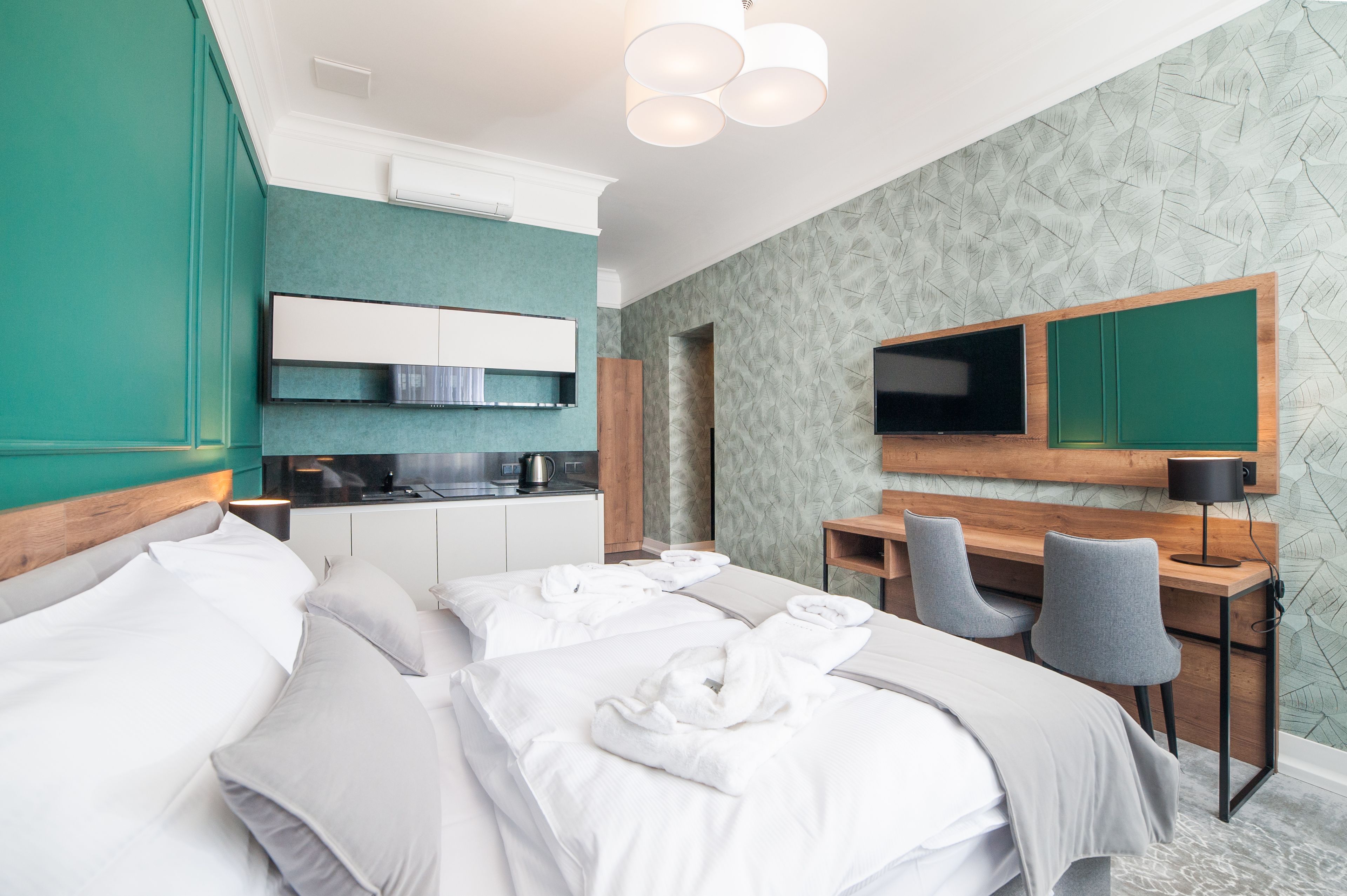 A hotel room with a bed, a desk with two chairs, a television, and a kitchenette.