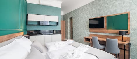 A hotel room with a bed, a desk with two chairs, a television, and a kitchenette.
