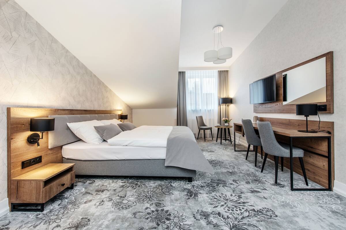 A modern hotel room with a large bed, a desk with chairs, a TV, and a large mirror.