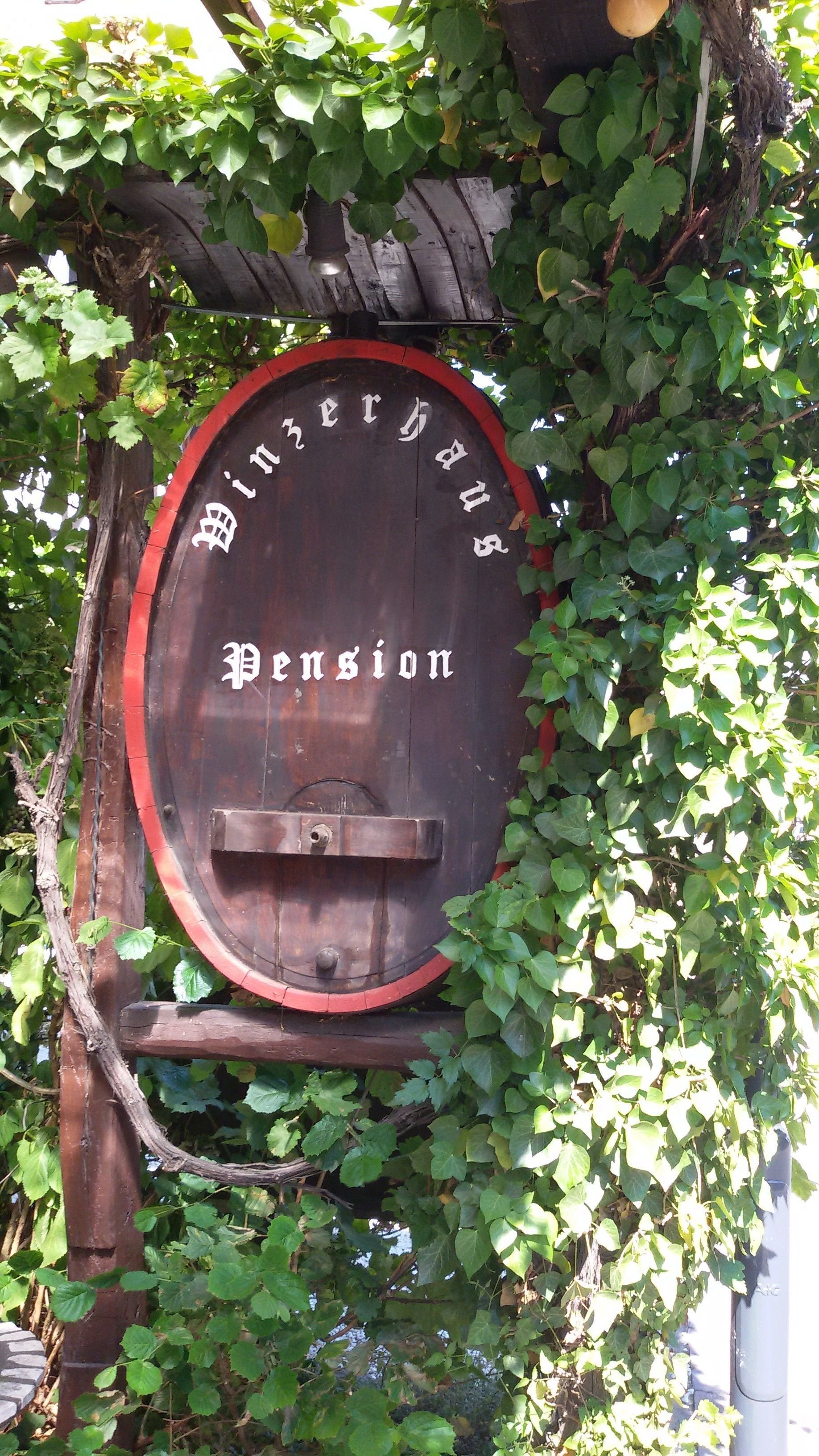 A wooden barrel with the inscription "Bierhaus Pension" surrounded by greenery.