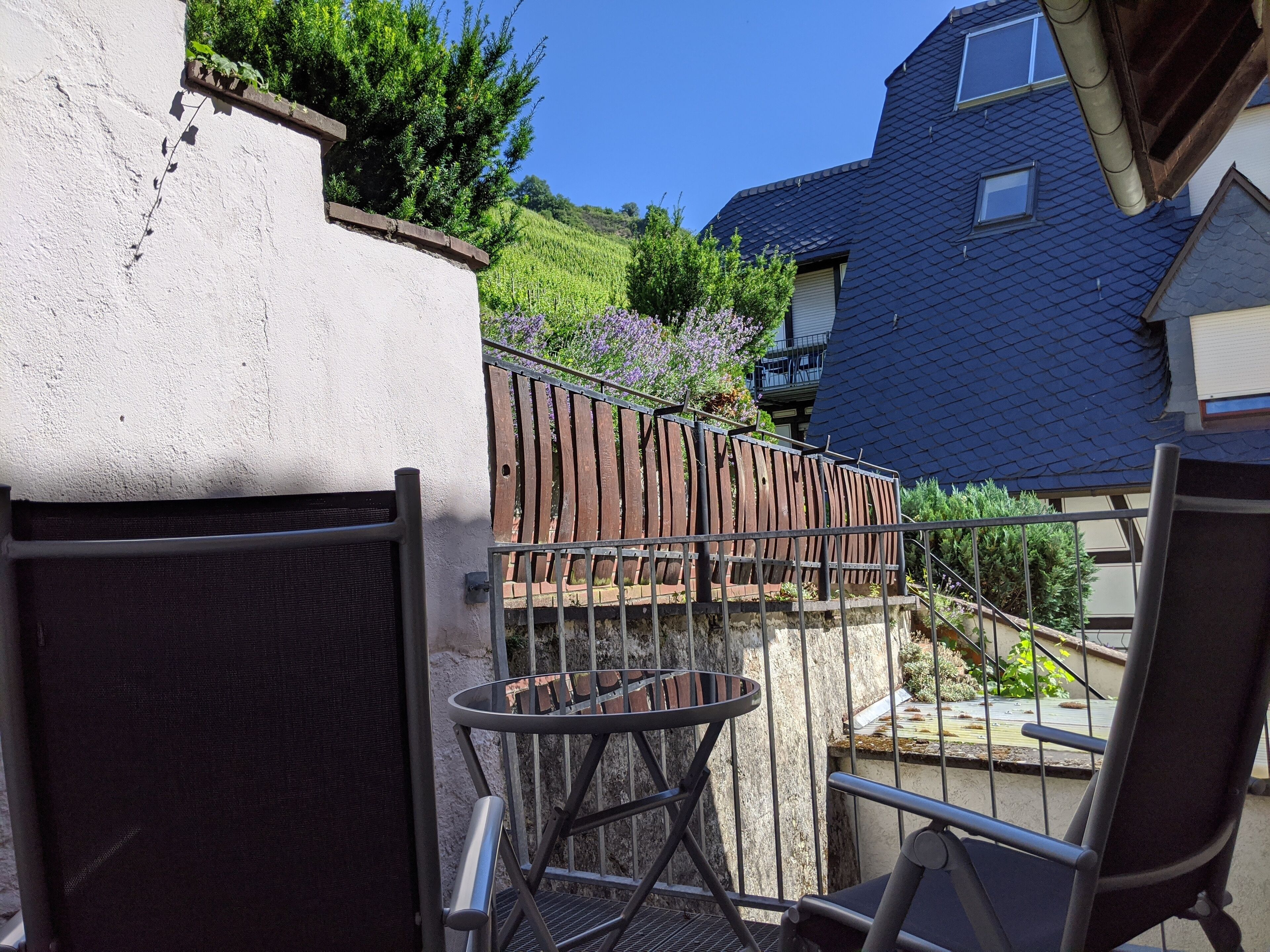 Un balcon avec une chaise et une table en métal, une clôture en bois et une vue sur une maison et la verdure.