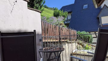 Un balcon avec une chaise et une table en métal, une clôture en bois et une vue sur une maison et la verdure.