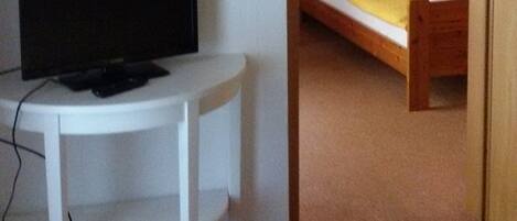 Una habitación pequeña con cama, escritorio y televisión.