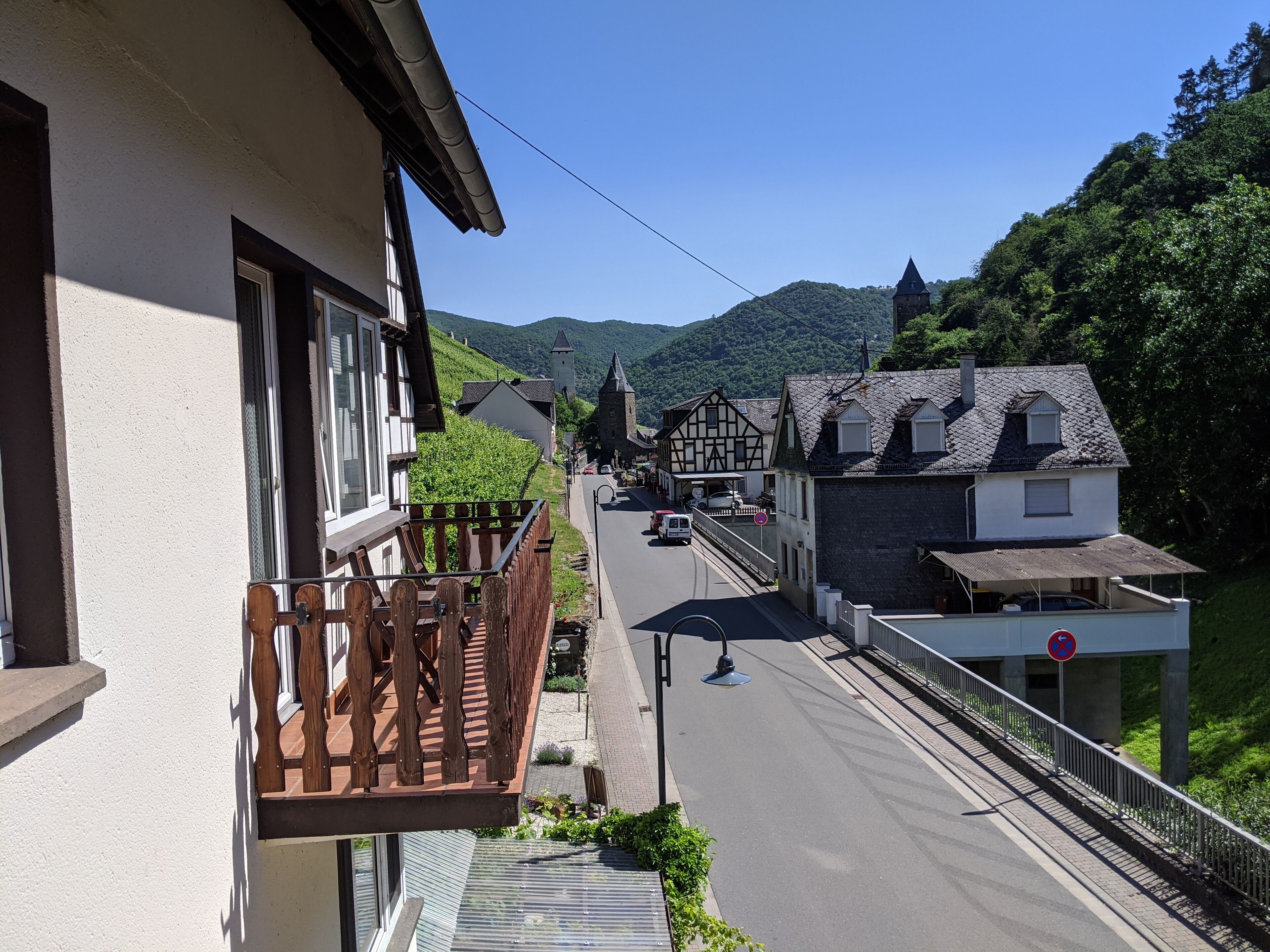 Een balkon met houten hekwerk met uitzicht op een straat vol traditionele gebouwen en een berg op de achtergrond.