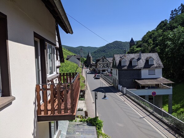 Ein Balkon mit Holzwertung, der auf eine Straße mit traditionellen Gebäuden und einem Berg im Hintergrund blickt.