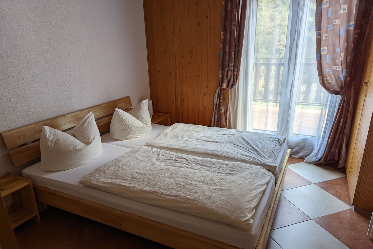 A double bed with white linens, wooden headboard, and pillows, in a room with wooden walls and a tiled floor.