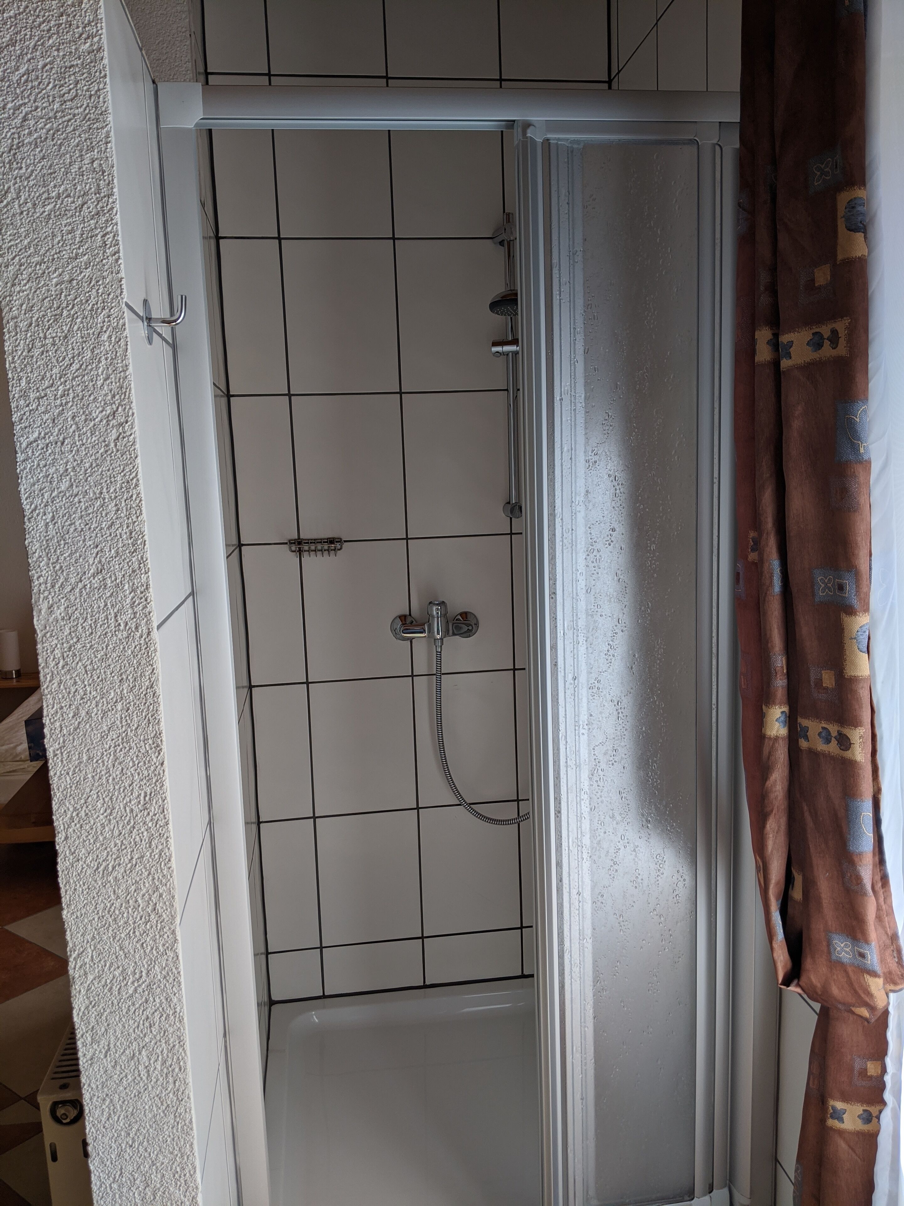 Un espace douche doté d’une porte en verre, de murs carrelés et d’un pommeau de douche.