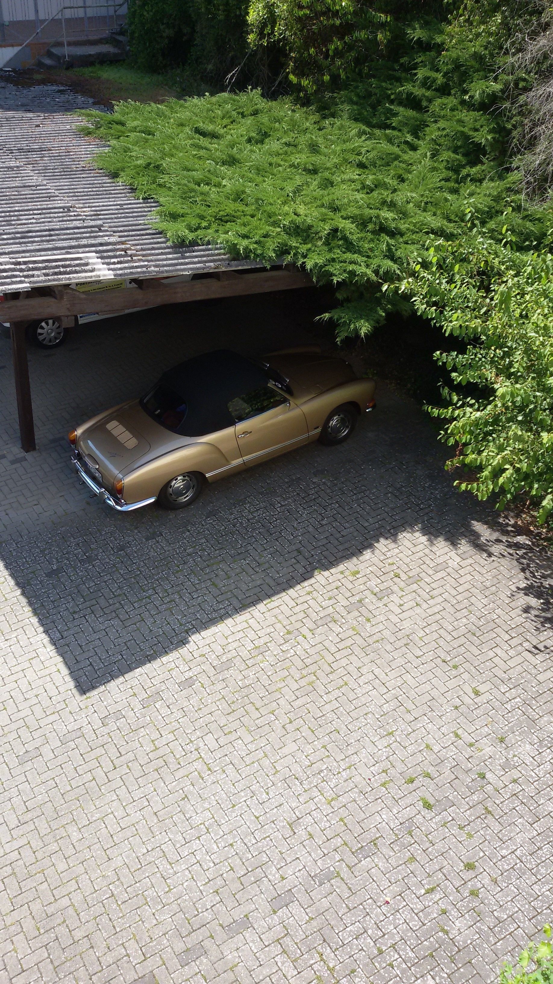 A vintage car parked under a covered area with a brick pavement.