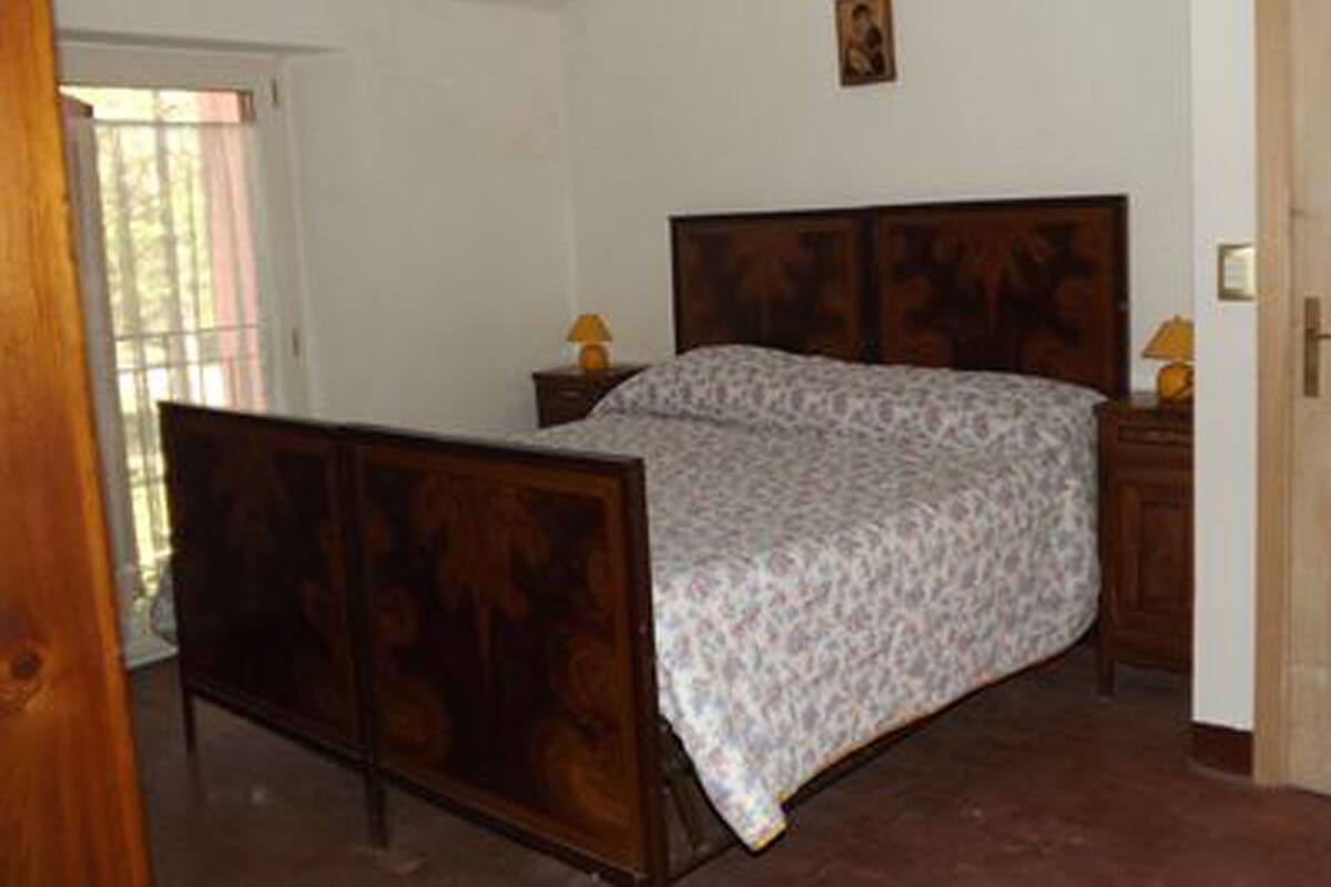 Ein Schlafzimmer mit einem hölzernen Bett, einem Nachttisch mit Lampe und einer Tür zu einem anderen Raum.