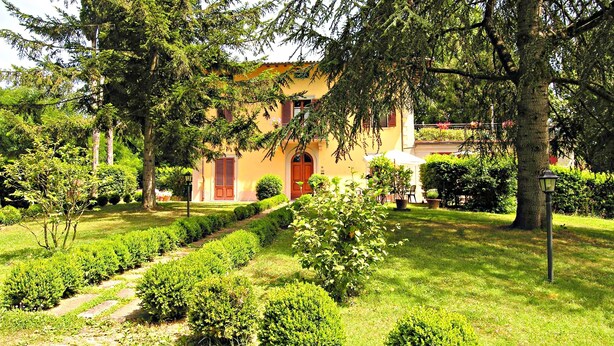 Un edificio con puerta roja, rodeado de jardines y árboles bien cuidados.