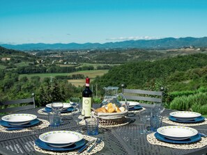 A table set for a meal with a bottle of wine, glasses, and bread, overlooking a scenic landscape. - Villa Eleonora (Dicomano)