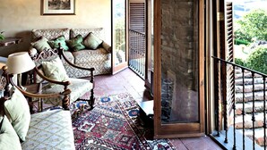A cozy living room with a patterned sofa, a wooden chair, and a rug. There is a balcony with a stone wall and a metal railing. - Villa Eleonora (Dicomano)