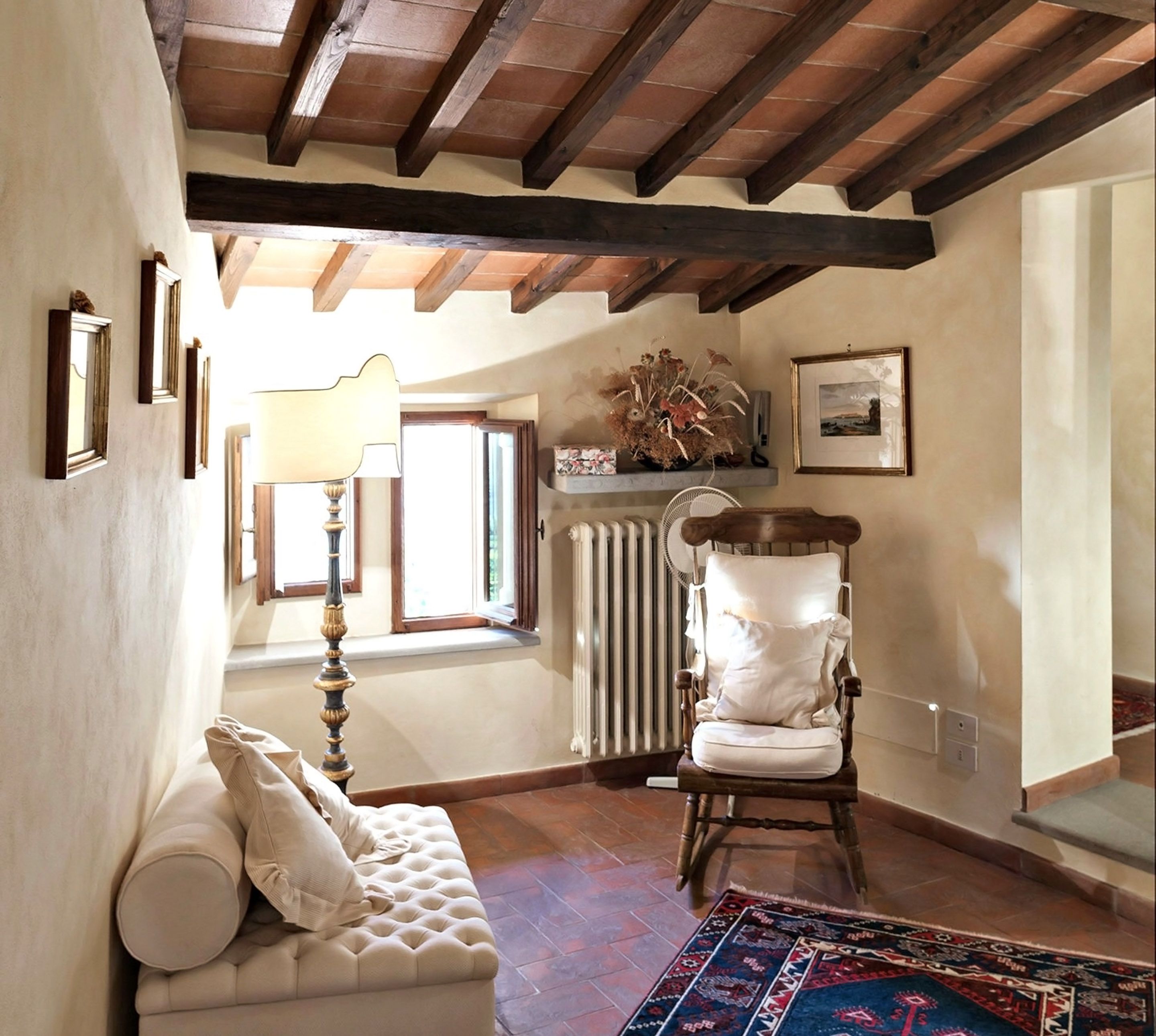 Une pièce chaleureuse avec un plafond en bois, un canapé blanc, un fauteuil et un tapis à motifs.