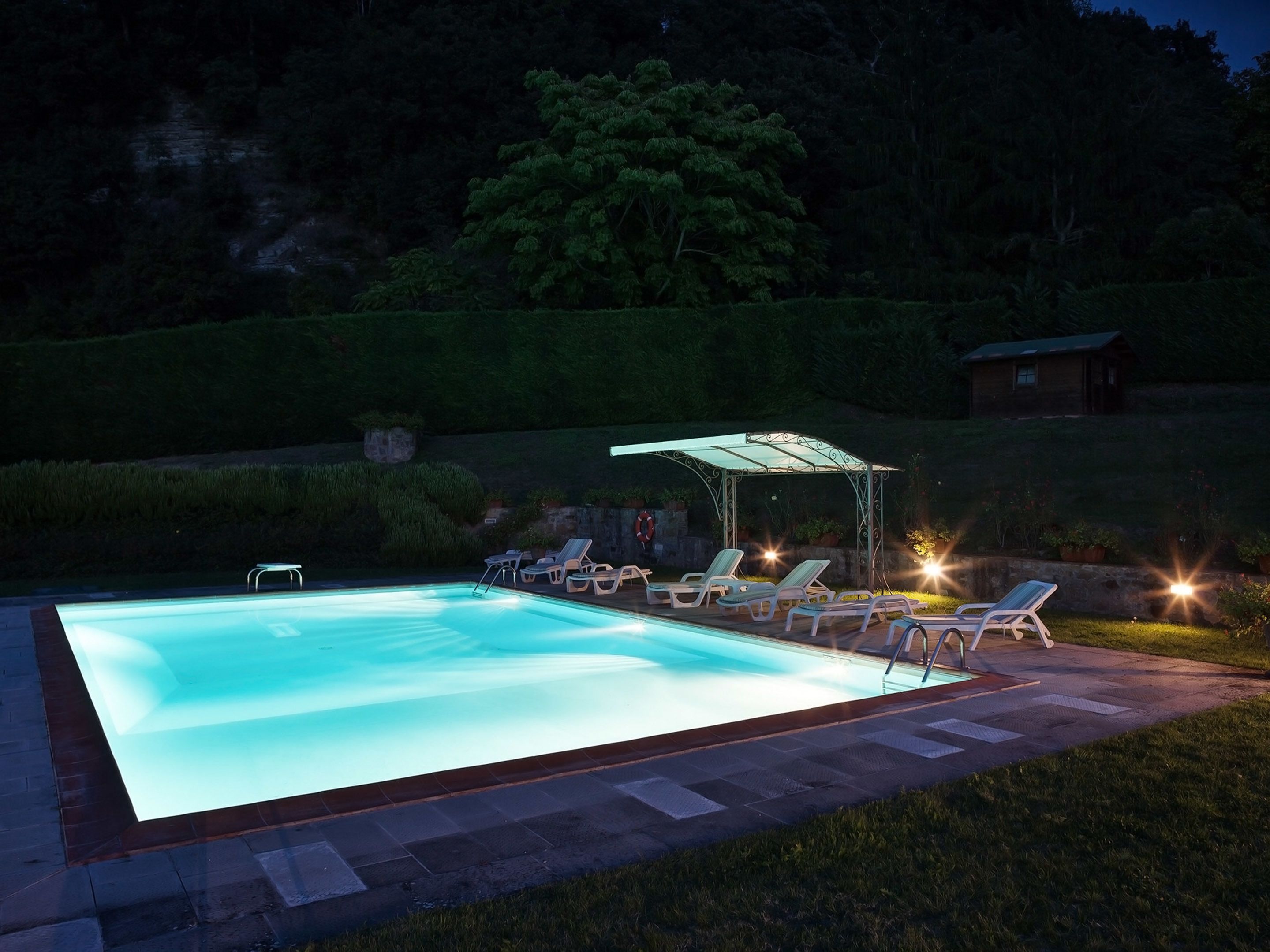 Una piscina con sillas de descanso y un área de estar techada.