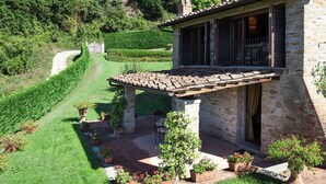 A stone house with a patio, surrounded by a well-maintained garden and a winding path. - Villa Eleonora (Dicomano)