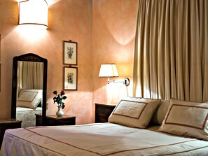 A hotel room with a large bed, a nightstand with a lamp, a mirror, and framed botanical prints on the wall. - Villa Eleonora (Dicomano)