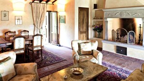 A cozy living room with a fireplace, floral-patterned furniture, and a dining area with a wooden table and chairs. - Villa Eleonora (Dicomano)