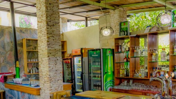 A bar area with a stone pillar, wooden ceiling, and shelves stocked with bottles and glasses. - Select Boutique Hotel (Kigali)