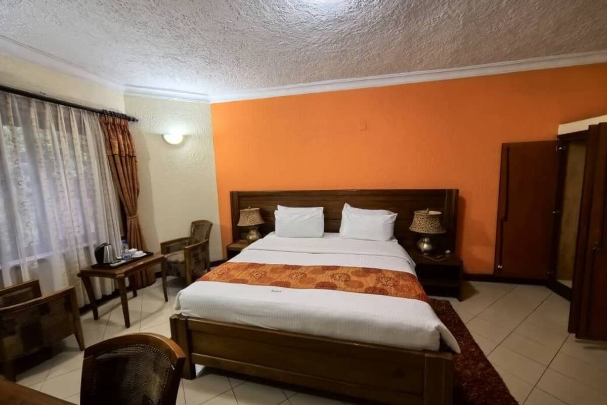 A hotel room with a wooden bed, two bedside tables with lamps, a chair, a desk, and a wardrobe.