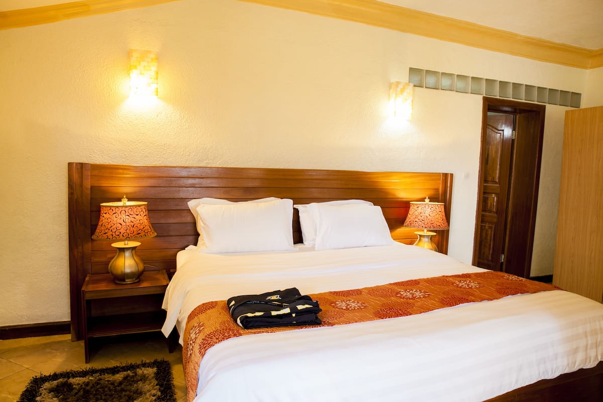 A hotel room with a wooden headboard, white bedding, two bedside lamps, and a neatly made bed with a folded jacket on the bed.